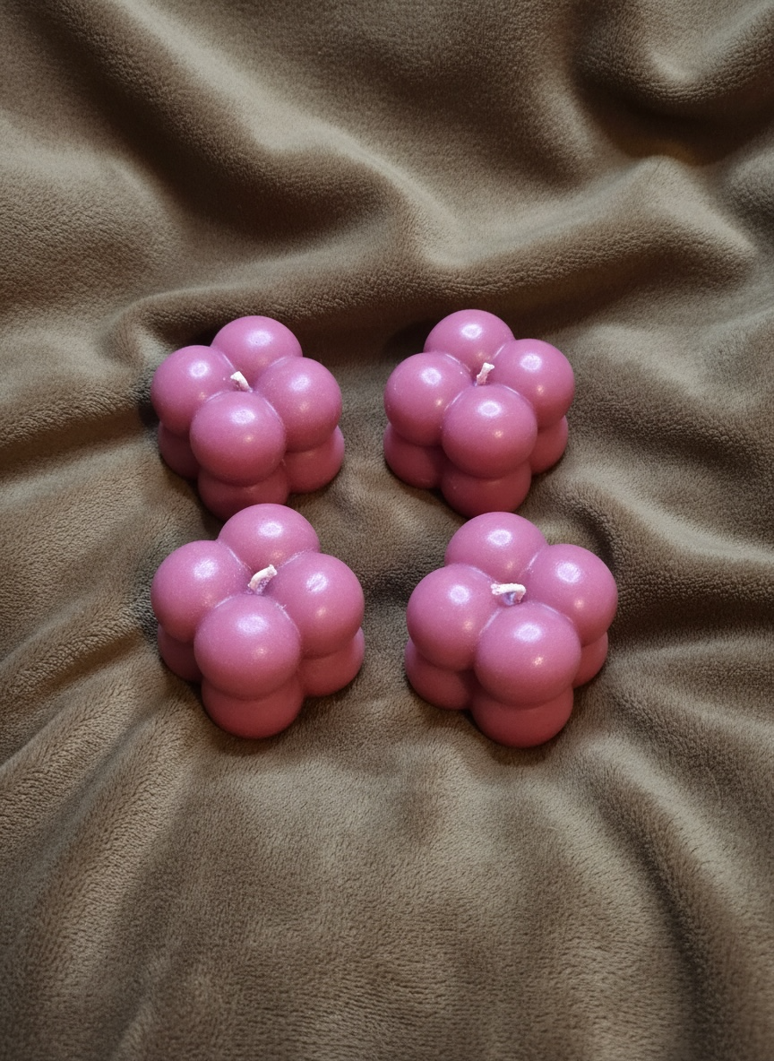 Four pink bubble-shaped candles on a brown fabric surface