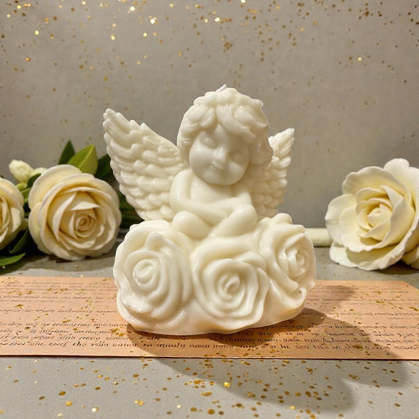 White angel candle figurine with wings sitting on a rose, surrounded by white roses on a textured surface.