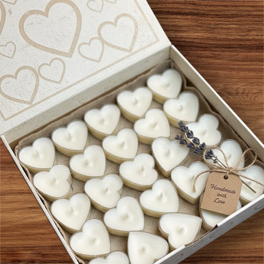 A box of 25 white heart-shaped soy wax tealight candles, hand-poured and packaged in a cream gift box with a rustic twine bow and a 'Handmade with Love' tag. Perfect romantic gift set.