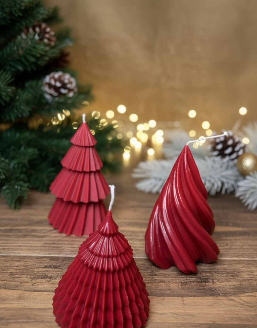 Red tree-shaped candles on a wooden surface with a blurred Christmas tree and lights in the background.