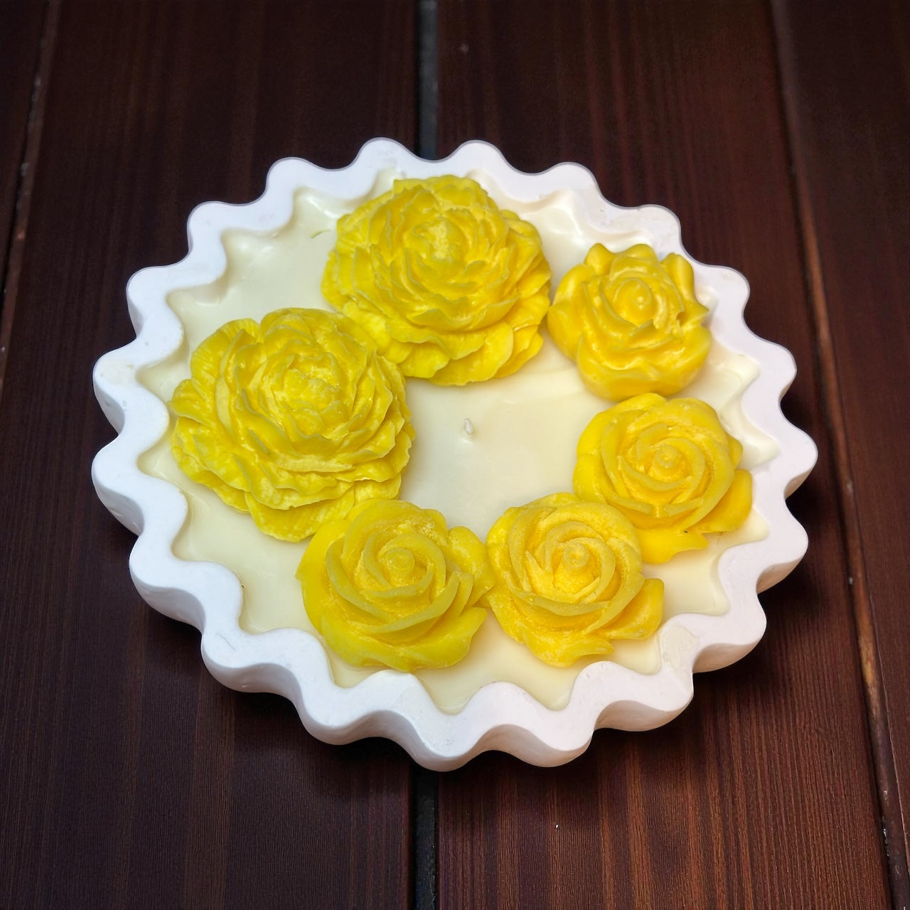 Scalloped Edge decorative candle with an asymmetrical grouping of bright yellow wax roses and dahlias. Floral soy wax centerpiece on a wooden windowsill."