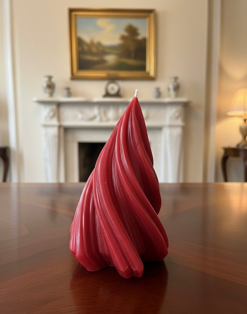 Decorative crimson red swirl pillar candle resting on a dark wood dining table in a stately room with an antique fireplace and framed painting in the background.