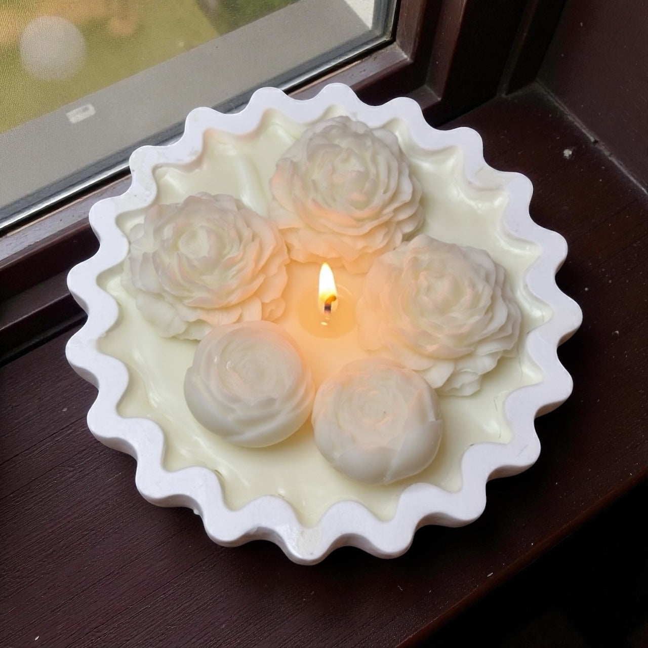 Lit Scalloped Edge decorative candle with four large white/ivory wax blossoms (ranunculus/peony style). Minimalist floral centerpiece for elegant home decor."