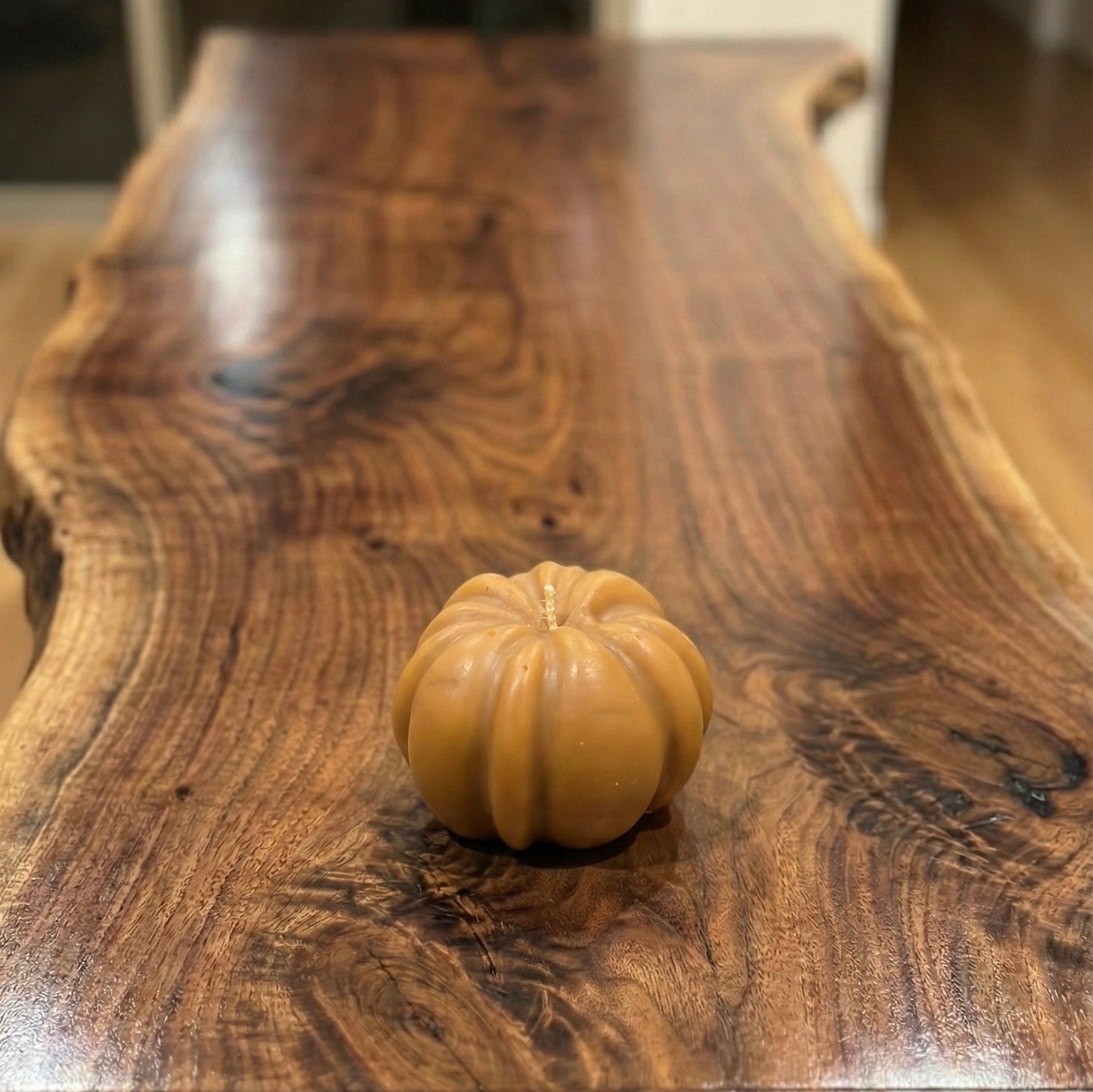 "Caramel-colored pumpkin-shaped candle sitting on a polished live-edge walnut table."