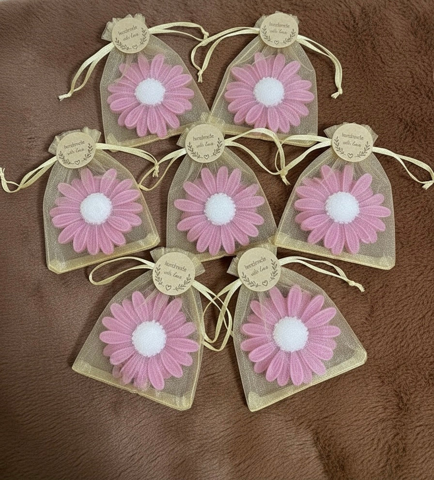 Seven handmade gerbera-shaped scented candles in bright pink with white centers, packaged in rustic yellow sheer organza gift bags with 'Handmade with Love' tags. Ideal pink party favours or baby shower thank you gifts