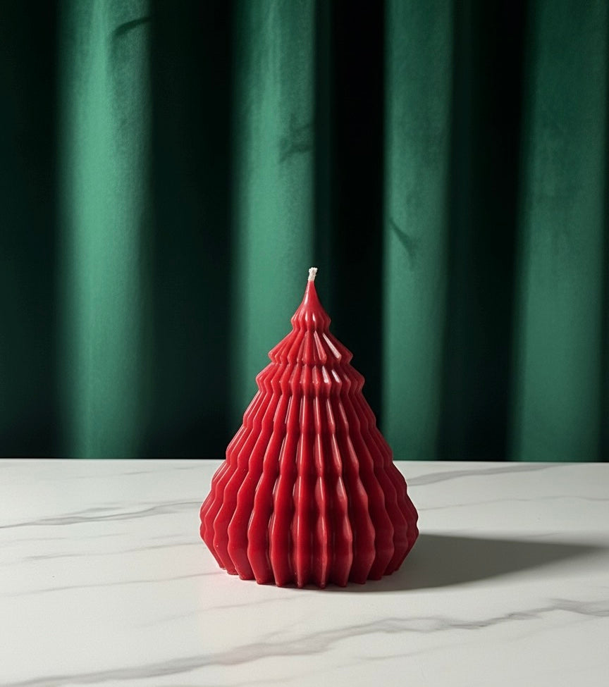 Striking festive red, corrugated Christmas tree-shaped candle displayed on a white marble surface with a deep green velvet curtain background.