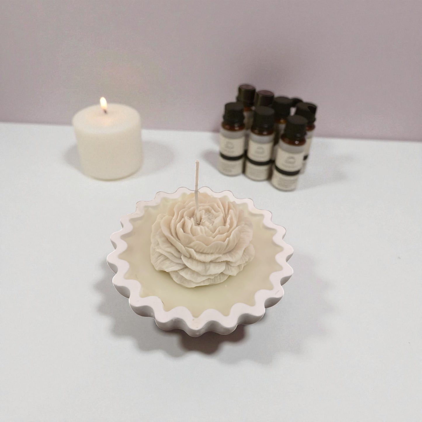 Unlit single pale white rose tart candle on a white surface with essential oil bottles.