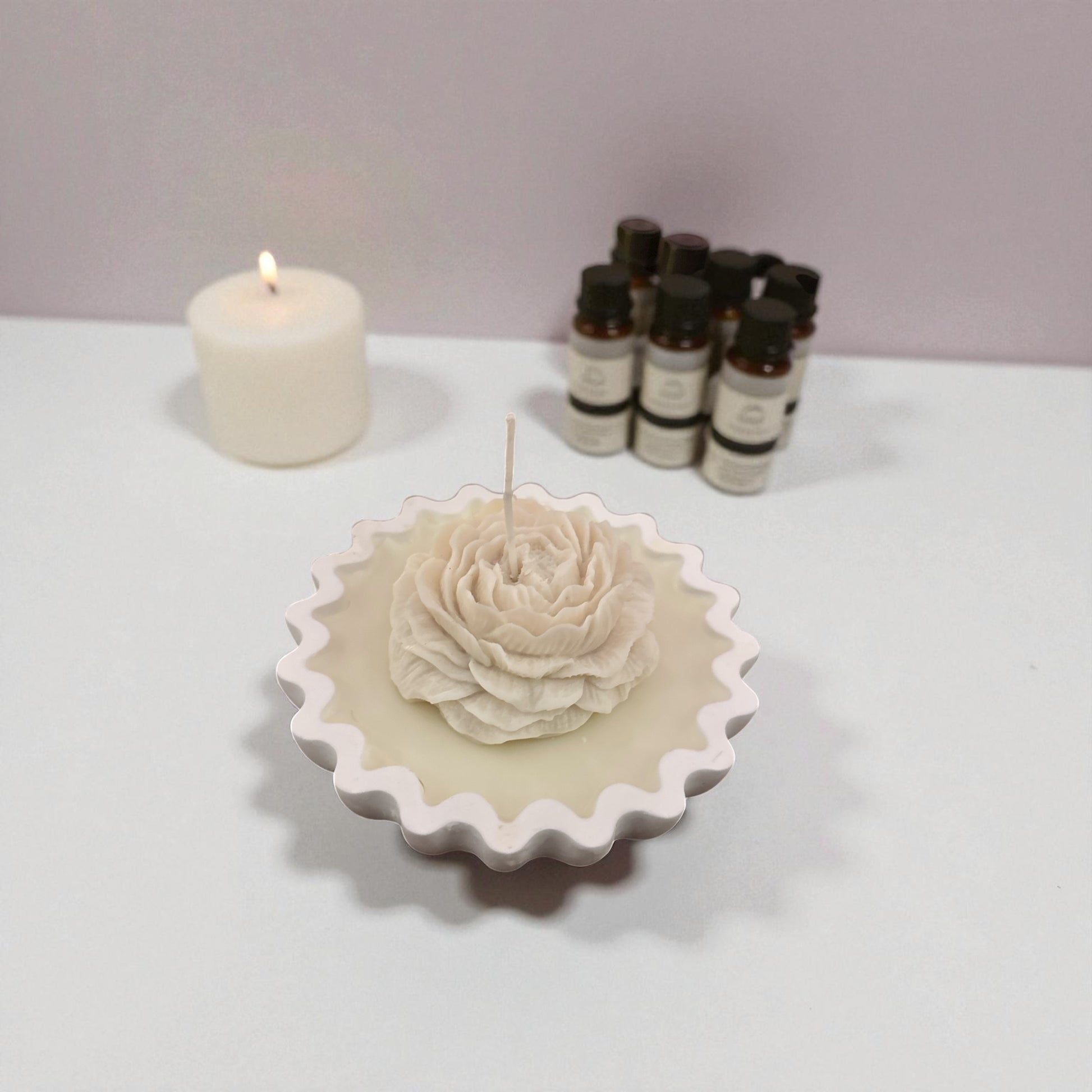 Unlit single pale white rose tart candle on a white surface with essential oil bottles.