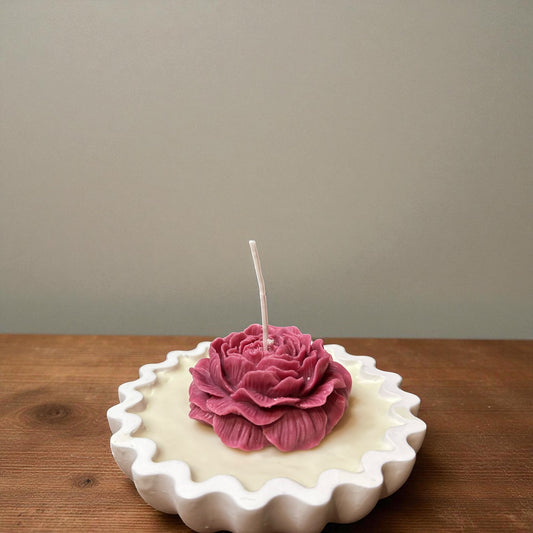 Unlit single pale pink rose tart candle on a white surface with essential oil bottles.