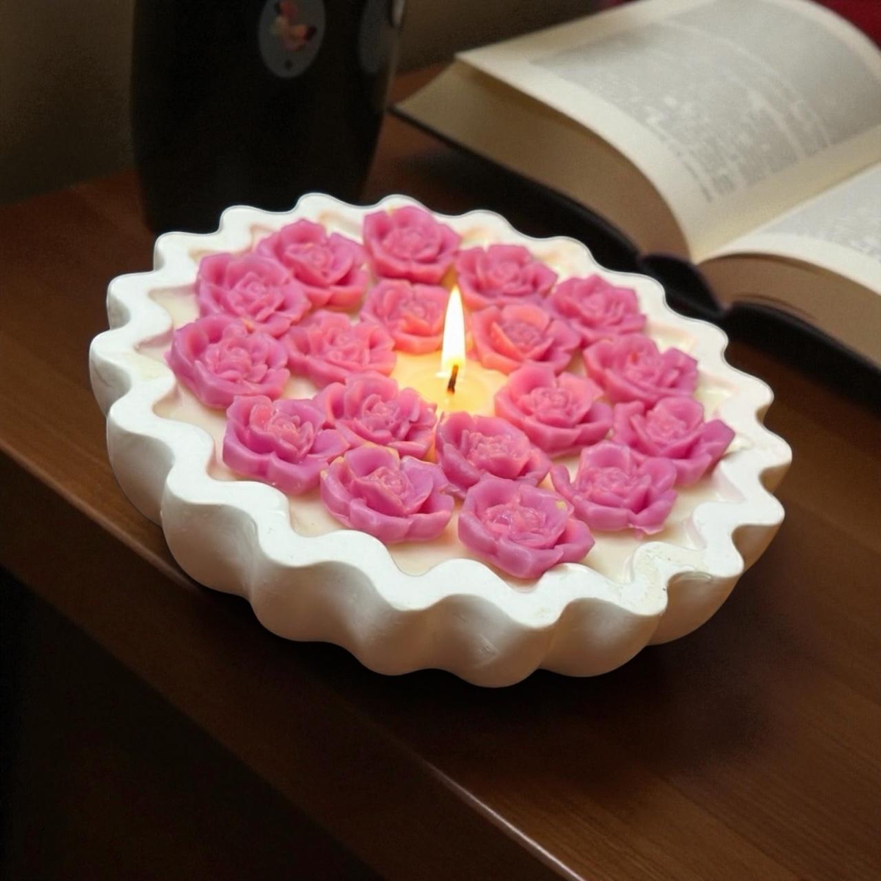 Lit pink rose tart candle on dark wood table with open book.