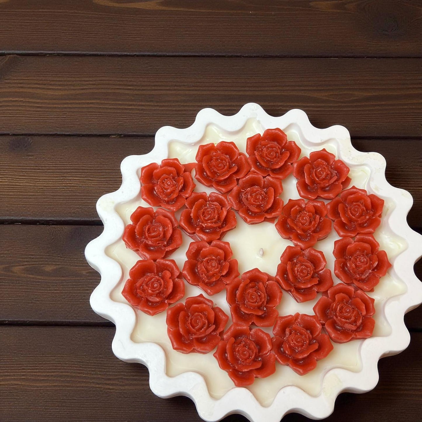 Close-up top view of unlit red rose tart candle on dark wood.